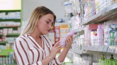 Güzel sarışın bir kadın dükkandaki kozmetik şişesine bakıyor.