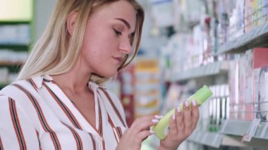 Güzel sarışın bir kadın dükkandaki kozmetik şişesine bakıyor.