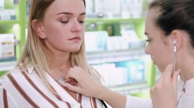 Kadın doktor ya da eczacı steteskoplu bir hastayı dinliyor.