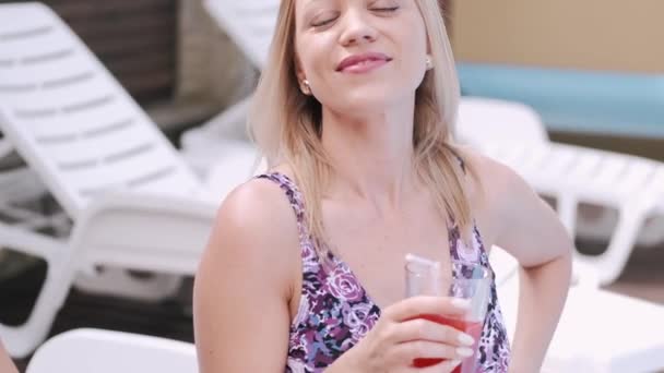 Красивая девушка пьет коктейль, стоя у бассейна — стоковое видео