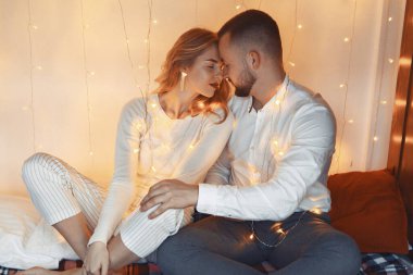 Zarif bir çift evde bir çelenk ile bir yatakta oturuyor.