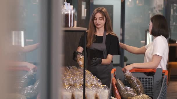Cliente mujer está eligiendo frutas secas en la tienda con un vendedor femenino — Vídeos de Stock