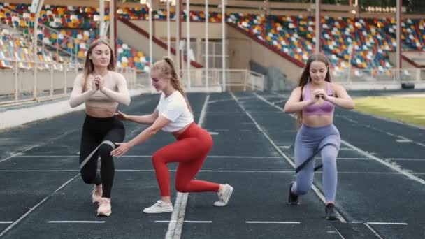 Sportovní ženy a trenérky dělat dřepy s odporem fitness gumové pásky na stadionu — Stock video