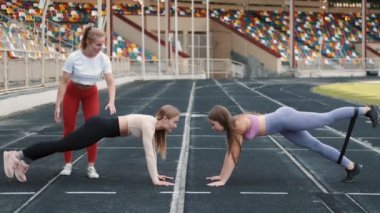 Spor kadınları ve koç stadyumdaki dayanıklılık bandıyla çömelme hareketleri yapıyorlar.