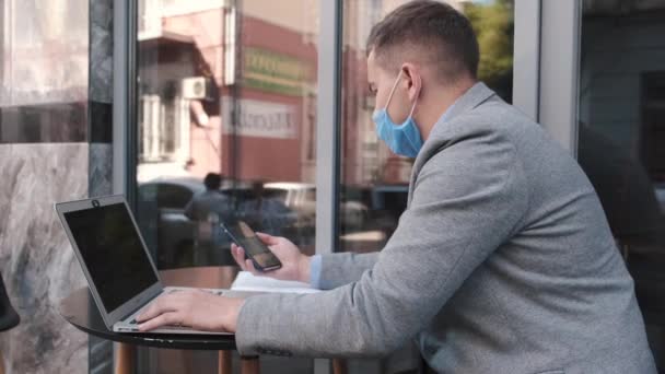 Hombre de negocios con máscara facial que trabaja con computadoras portátiles en la cafetería — Vídeo de stock