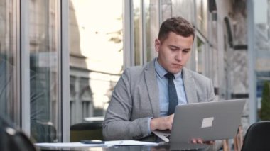 Takım elbiseli bir iş adamı kafede dizüstü bilgisayar kullanıyor.