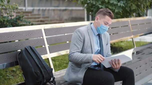Obchodník v jednorázové masce čte papíry na lavičce — Stock video