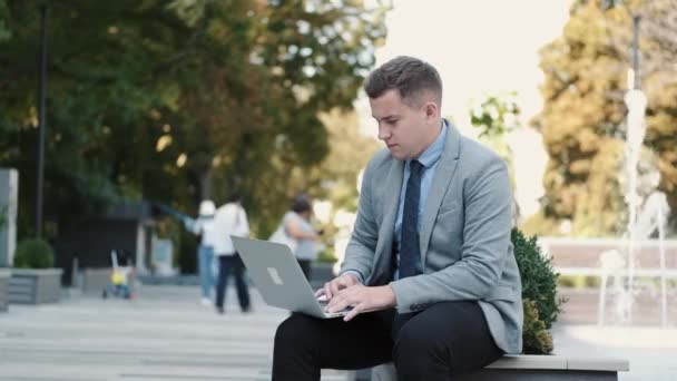 Hombre de negocios en traje usando un portátil en un parque público — Vídeos de Stock