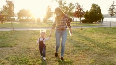 Genç anne küçük kızıyla halka açık bir parkta yürüyor.