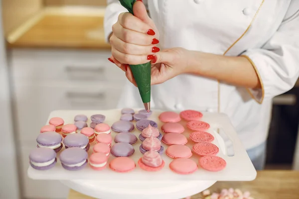 Confectioner in a uniform decorates the macaroni