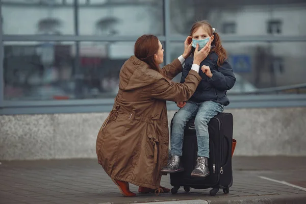 Una madre europea en un respirador con su hija está de pie cerca de un edificio.El padre le está enseñando a su hijo a usar máscara protectora para salvarse del virus. —  Fotos de Stock