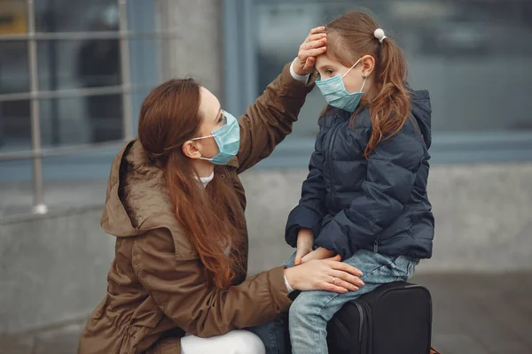 Una madre europea en un respirador con su hija está de pie cerca de un edificio.El padre le está enseñando a su hijo a usar máscara protectora para salvarse del virus. — Foto de Stock