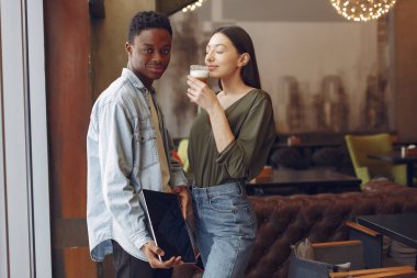 Bir kafede elinde tablet ve kahveyle duran uluslararası insanlar.