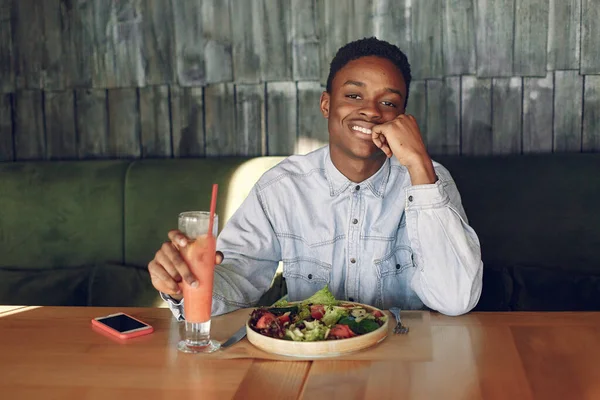 Black man sitting in a cafe and eating a vegetable salad