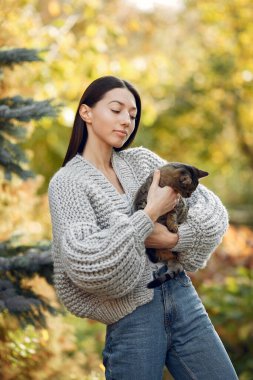 Örgü kazaklı bir kız ağaçların arkasında dikiliyor.