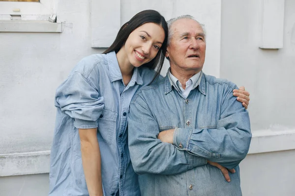 Старий стоїть на сірому фоні зі своєю онукою — стокове фото
