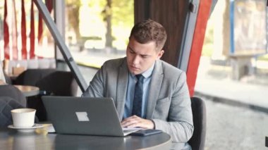 Takım elbiseli bir iş adamı kafede dizüstü bilgisayar kullanıyor.