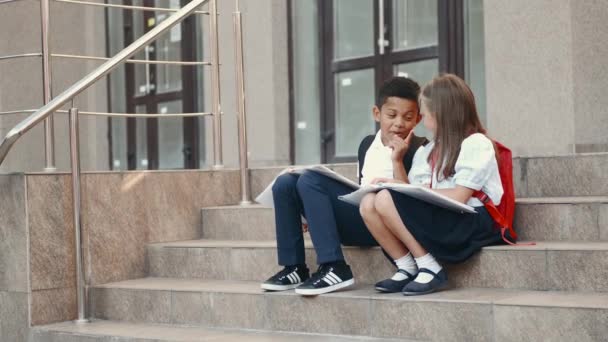 Niños de la escuela leyendo libro mientras están sentados en escaleras — Vídeo de stock