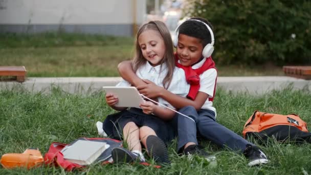 Murid yang lucu menggunakan notebook dan mendengarkan musik duduk di rumput — Stok Video