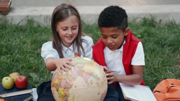 Учні дивляться на глобус, що сидить на траві після школи — стокове відео