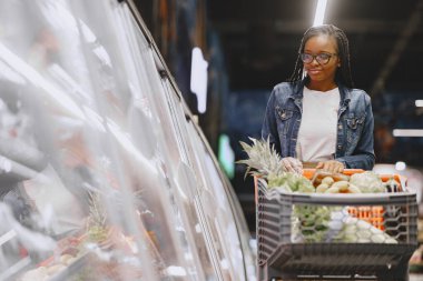 Kadın süpermarkette sebze alışverişi yapıyor.