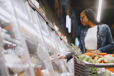 Kadın süpermarkette sebze alışverişi yapıyor.