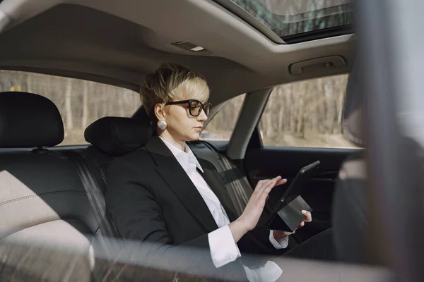 Empresaria sentada dentro de un coche y usando una tableta — Foto de Stock