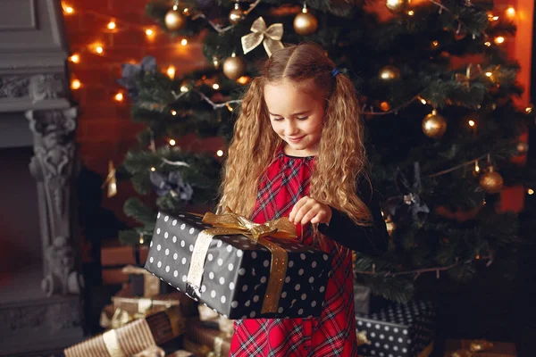 Маленькая девочка, стоящая рядом с елкой с подарком — стоковое фото