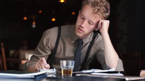 悲しいビジネスマンがウイスキーと紙を読んでテーブルに座って — ストック動画