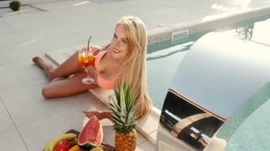 Güzel düz göbekli, bikinili kadın havuz kenarında uzanıyor ve güneşli günün tadını çıkarıyor.