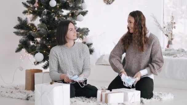 Two attractive women sitting udr th Christmas tree and throwing masks in the air — Stock Video