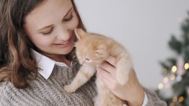 Uśmiechnięta młoda kobieta gra z kotkiem przeciwko choince — Wideo stockowe