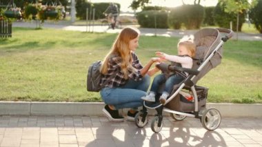 Genç bir anne ve kızı bebek arabasında iletişim kuruyor.