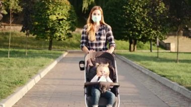 Genç anne halka açık bir parkta elinde bebek arabasıyla yürüyor.