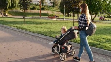 Genç anne halka açık bir parkta elinde bebek arabasıyla yürüyor.