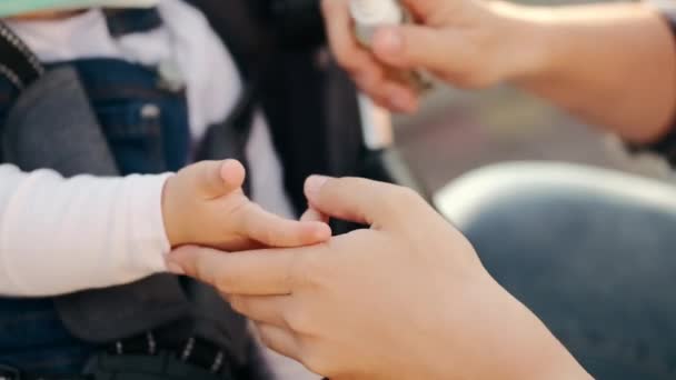 Vrouw desinfecteert haar dochters handen buiten — Stockvideo