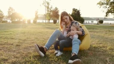 Anne ve kızı gün batımında bir yaz parkında puf koltukta oynuyorlar.