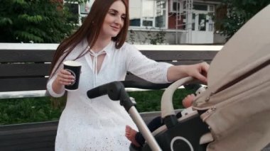 Kahve ve bebek arabasıyla bankta oturan güzel bir anne.