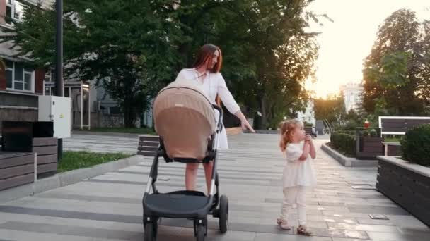 Krásná matka procházky s kočárkem a malou dceruškou na chodníku ve městě — Stock video