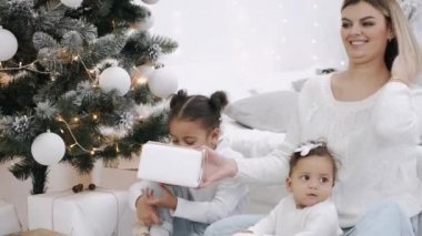 Anne kızlarıyla birlikte Noel ağacının altında hediyelerle oturuyor.