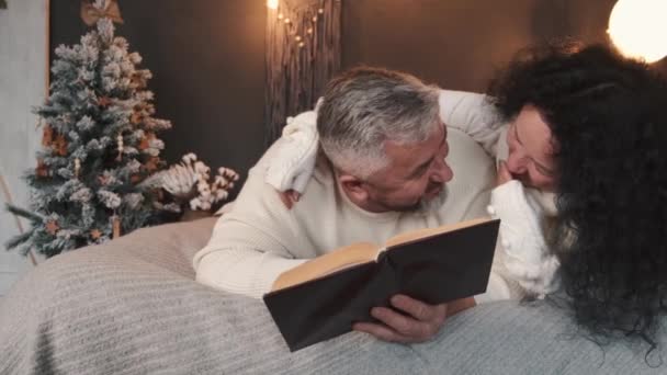Старша пара читає і відпочиває на ліжку в різдвяній атмосфері. — стокове відео