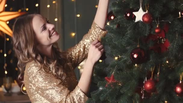 Pretty young lady in elegant dress decorating xmas tree for new years party — Stock Video