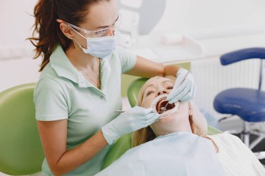 Diş hekimi eski hastasına aletlerle bakıyor.