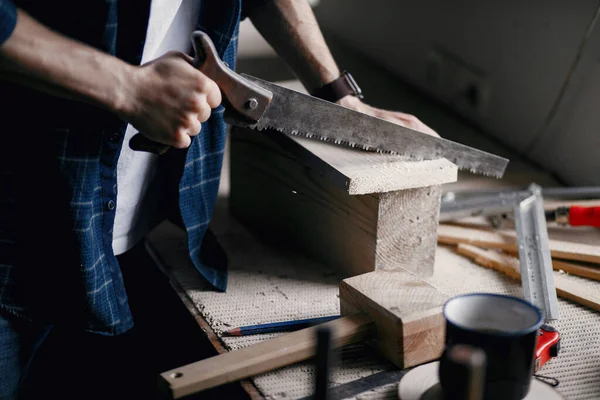 Man in the workshop with a wood and saw — Stock Photo, Image