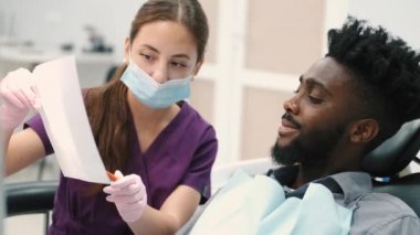 Kadın bir dişçi hastalara dişlerinin röntgenini gösterir ve bunu tartışır.