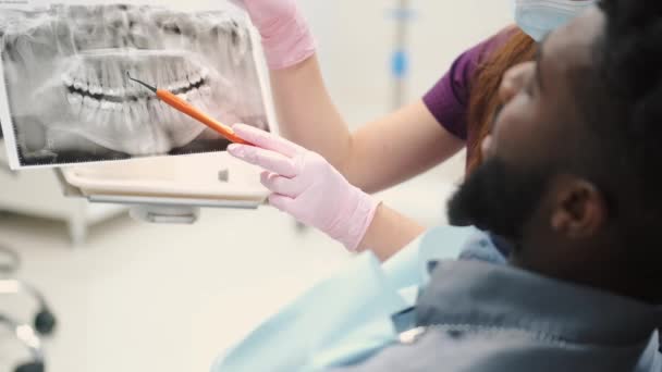 Žena zubařka ukazuje pacientům rentgen zubů a diskutuje o tom — Stock video