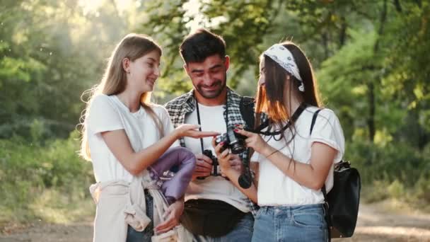Três jovens olham para a exibição de câmeras na floresta — Vídeo de Stock