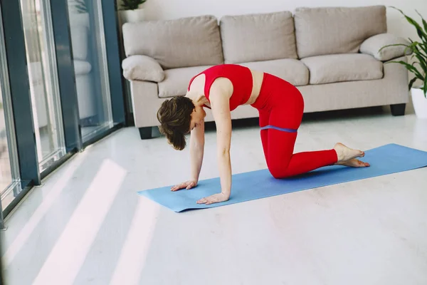 Девушка в красной спортивной форме делает йогу дома — стоковое фото