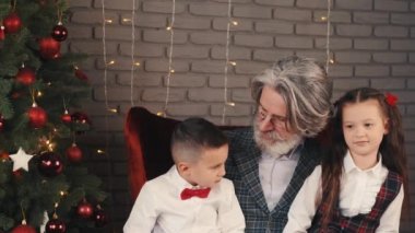 Dedem ve çocuklar Noel ağacının yanındaki kanepede oturuyorlar.