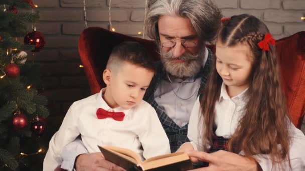Παππού και παιδιά διαβάζουν ένα βιβλίο την παραμονή των Χριστουγέννων — Αρχείο Βίντεο